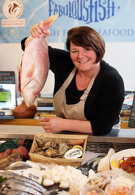 A woman holding up a pink fish leaning on a fish counter.