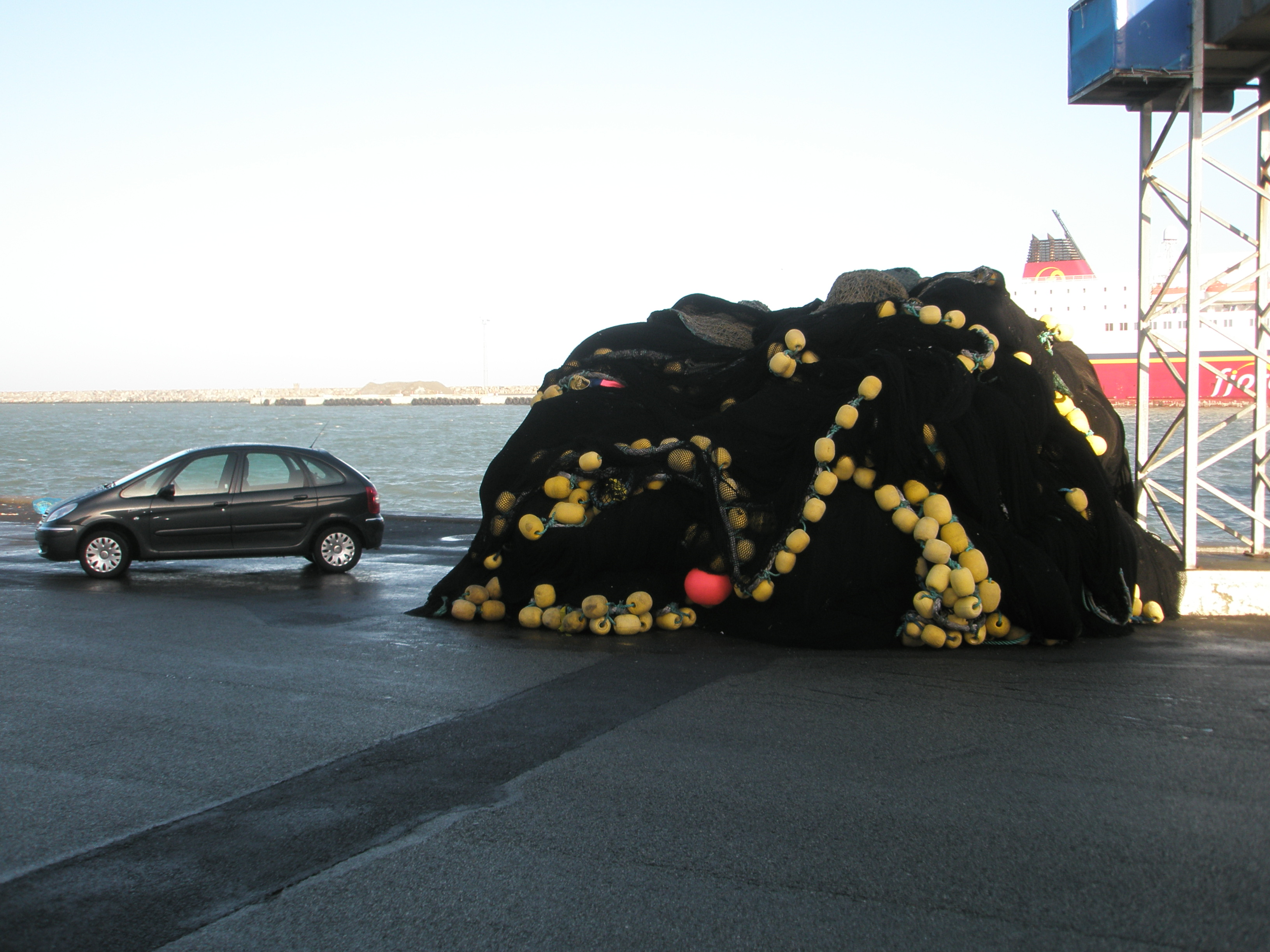 A purse seine net on harbourside next to a car