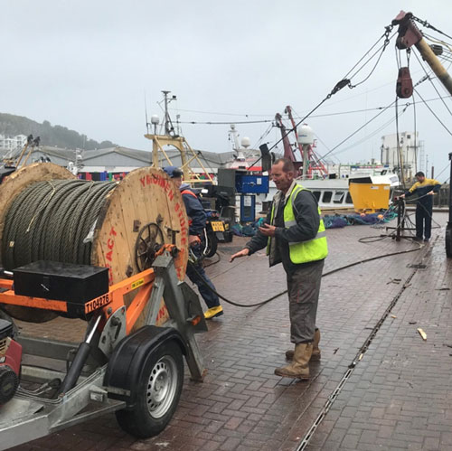 Photo of Edd on pier working with large wire reel on trailer