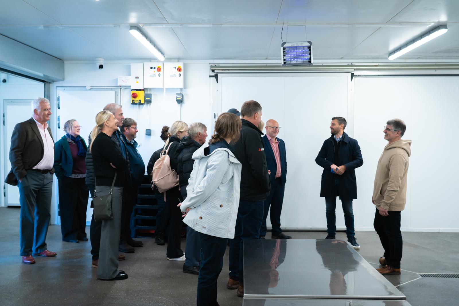 People gathered listening to a speaker on a tour inside a fish processing unit.