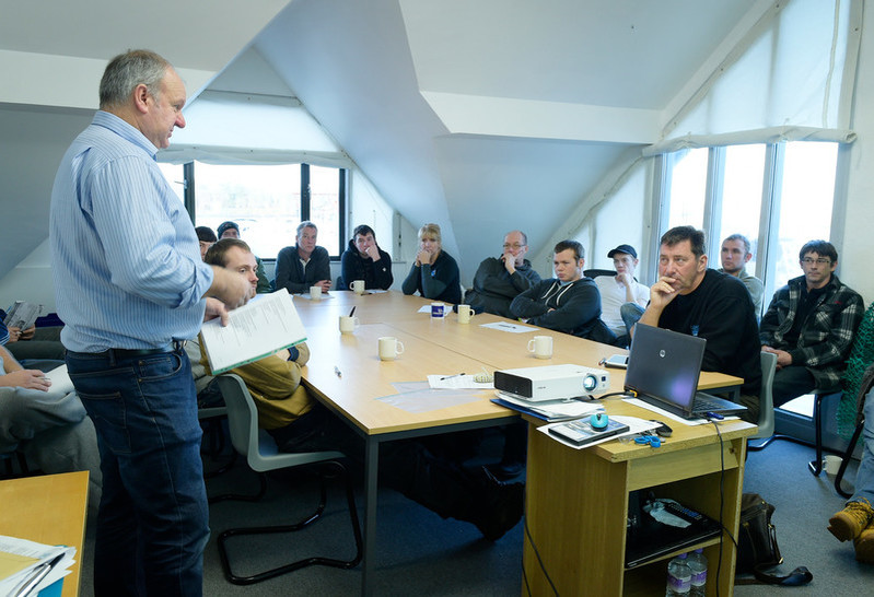 A fishing safety advisor is talking to a group of men in a classroom