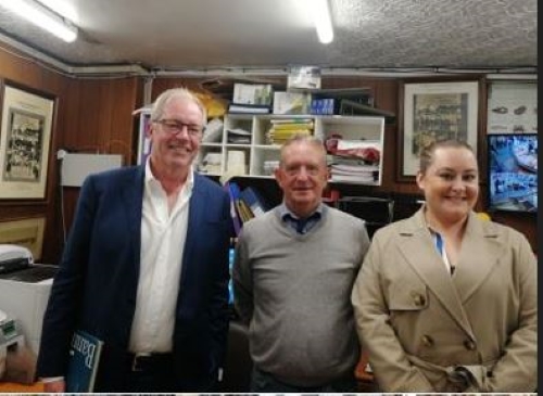 Three people, including Graham Black on the left, standing smiling together in a room