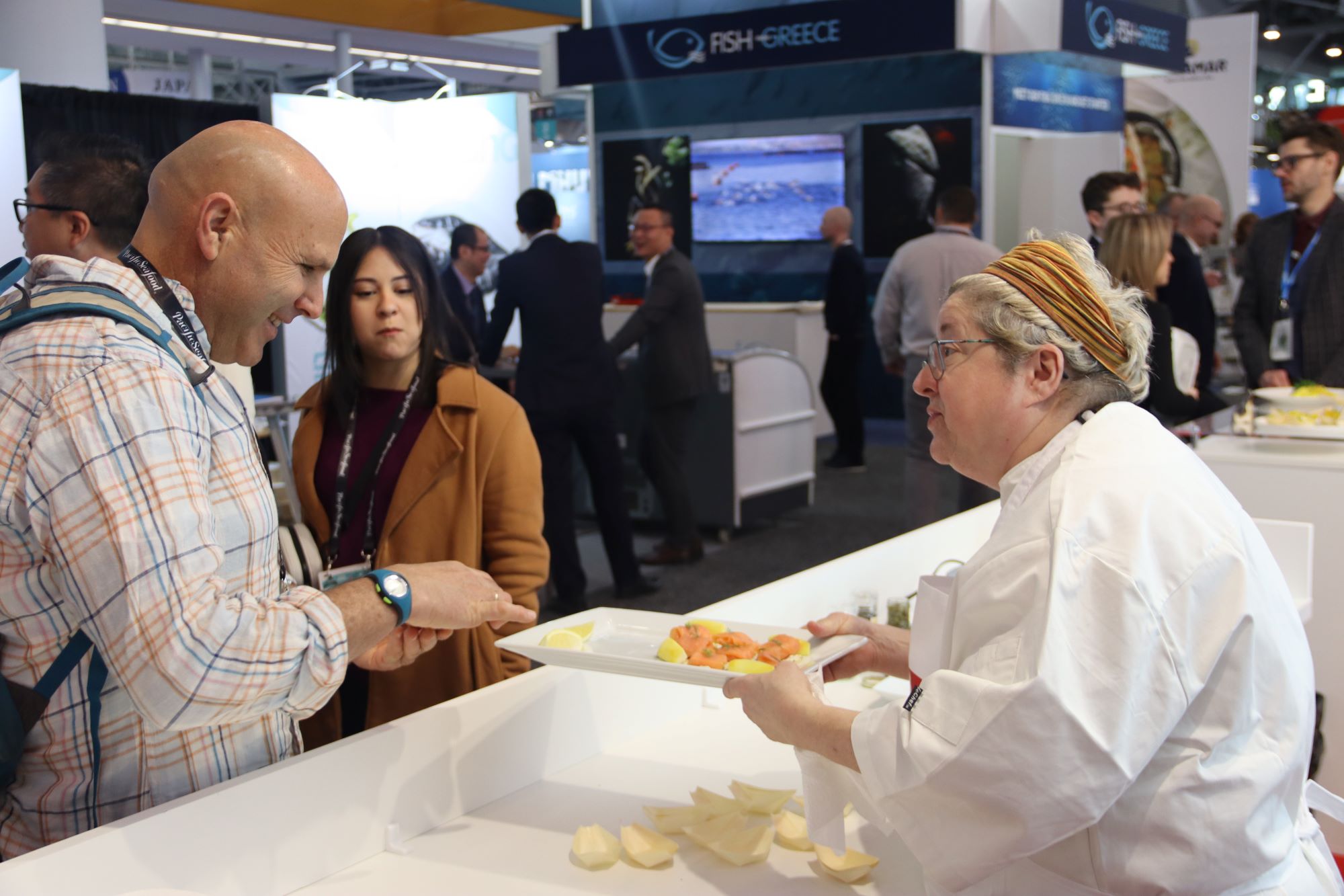 A chef presents a tray of seafood samples to an attendee at a trade show.