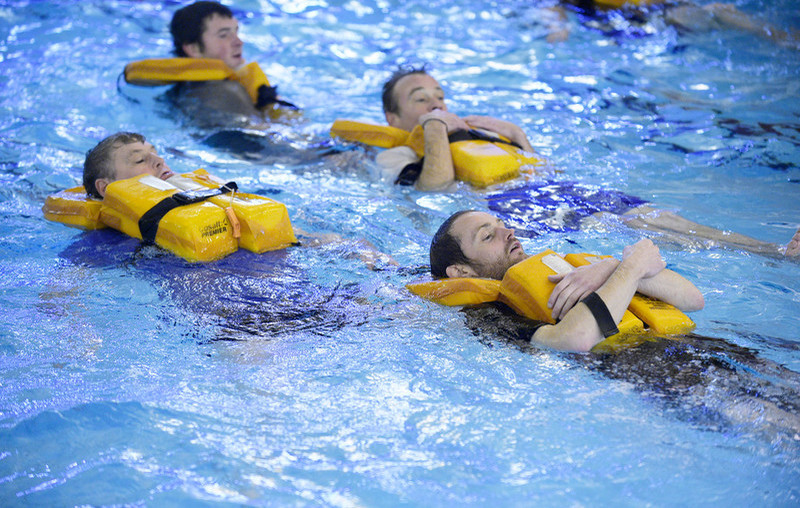 A group of men with flotation devices are floating on their backs in a swimming pool.