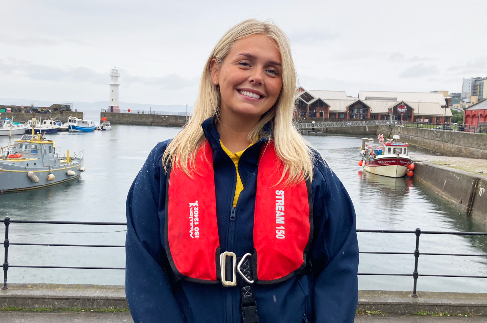 Field Researcher Emma at a harbour in front of fishing boats.