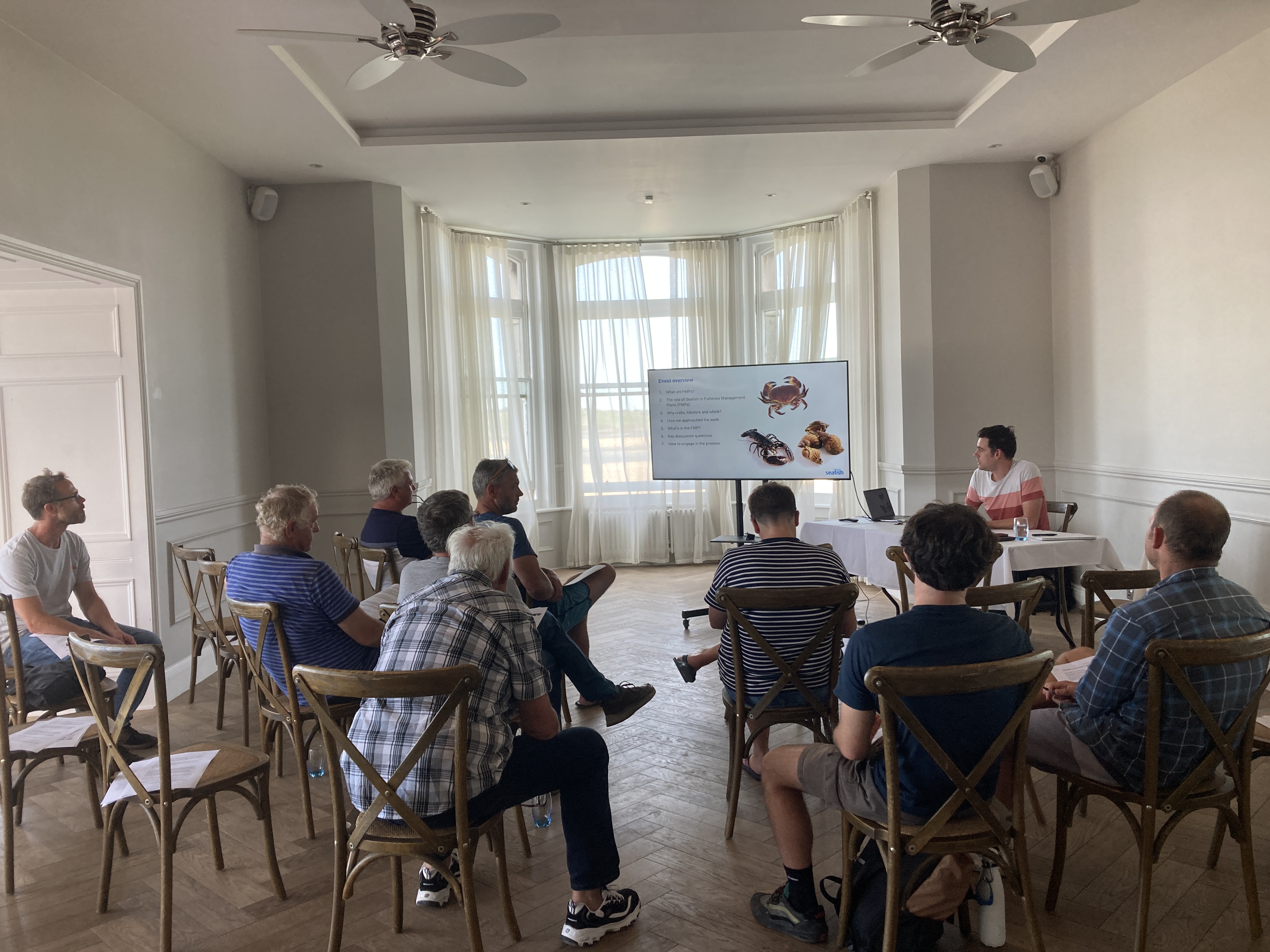 A group of people sitting in a room, looking at a presentation on a television screen