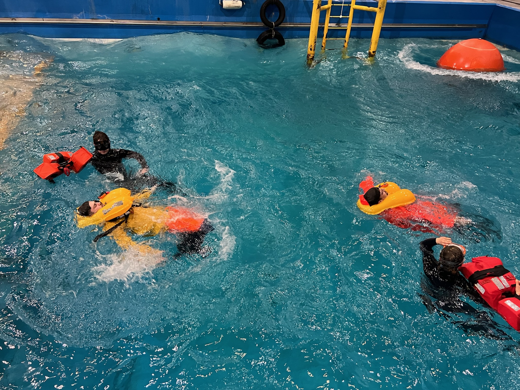 A group of men in a training swimming pool with flotation devices on as part of a training exercise.