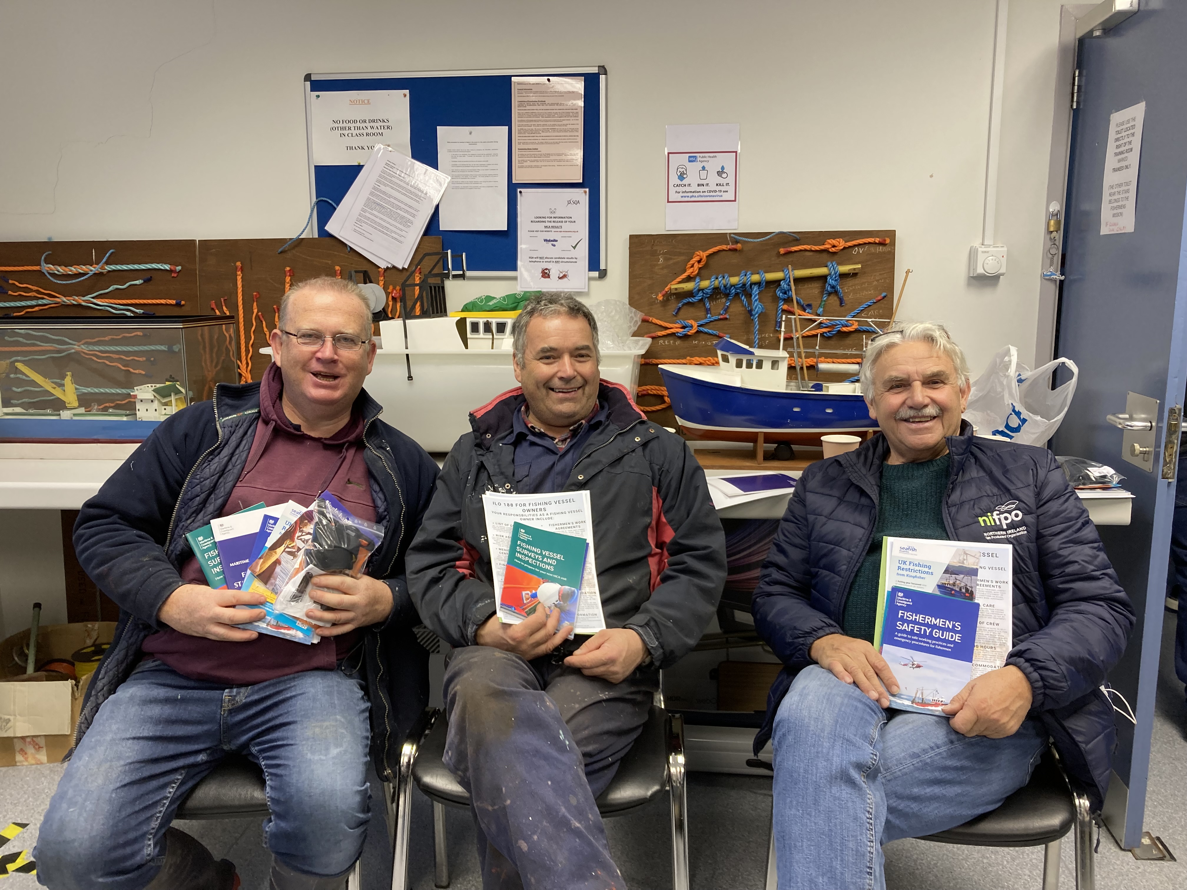 Three men sitting together holding fishing safety materials