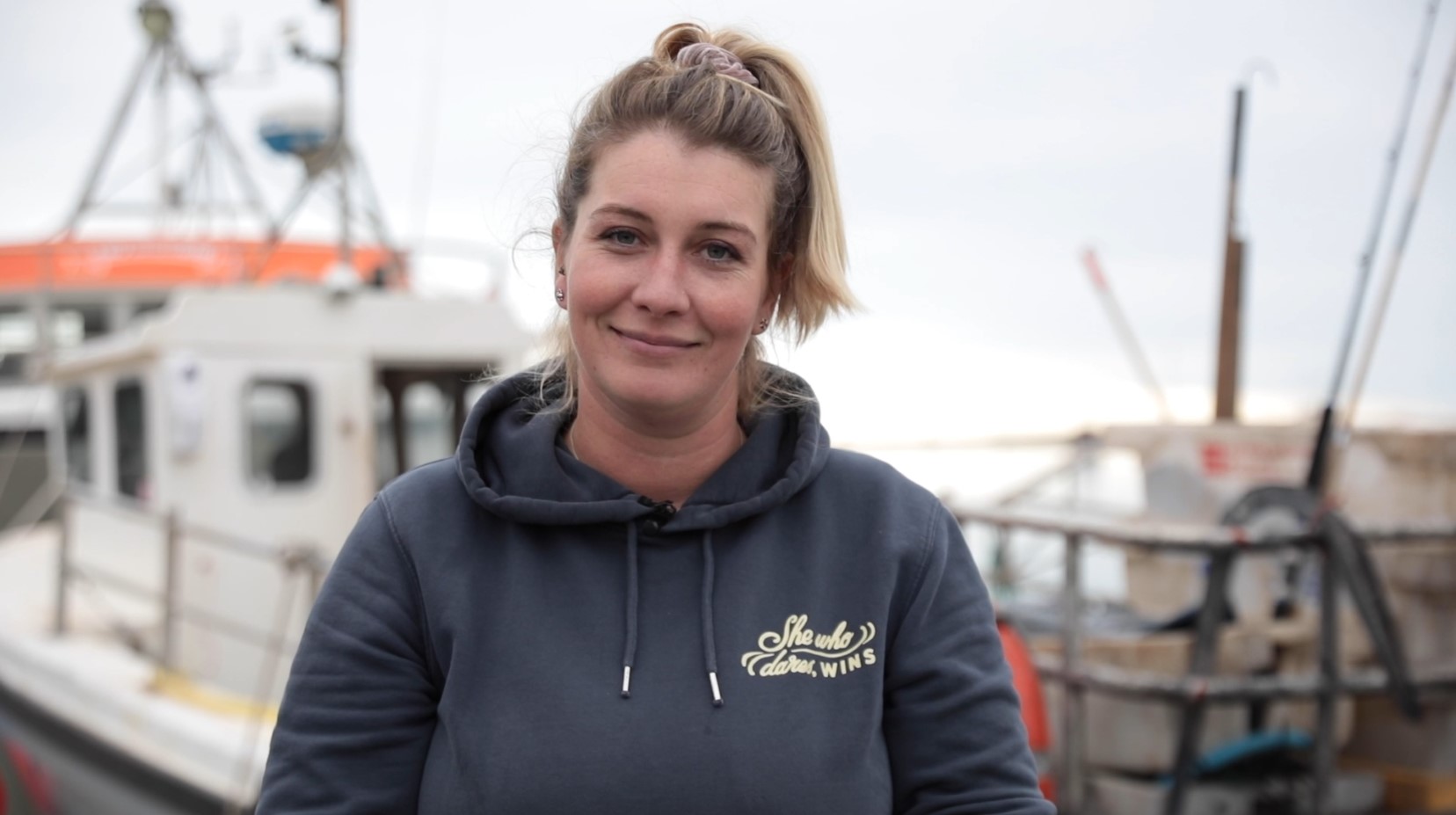 Photo shows fisher Ashley Mullenger standing in front of a fishing vessel