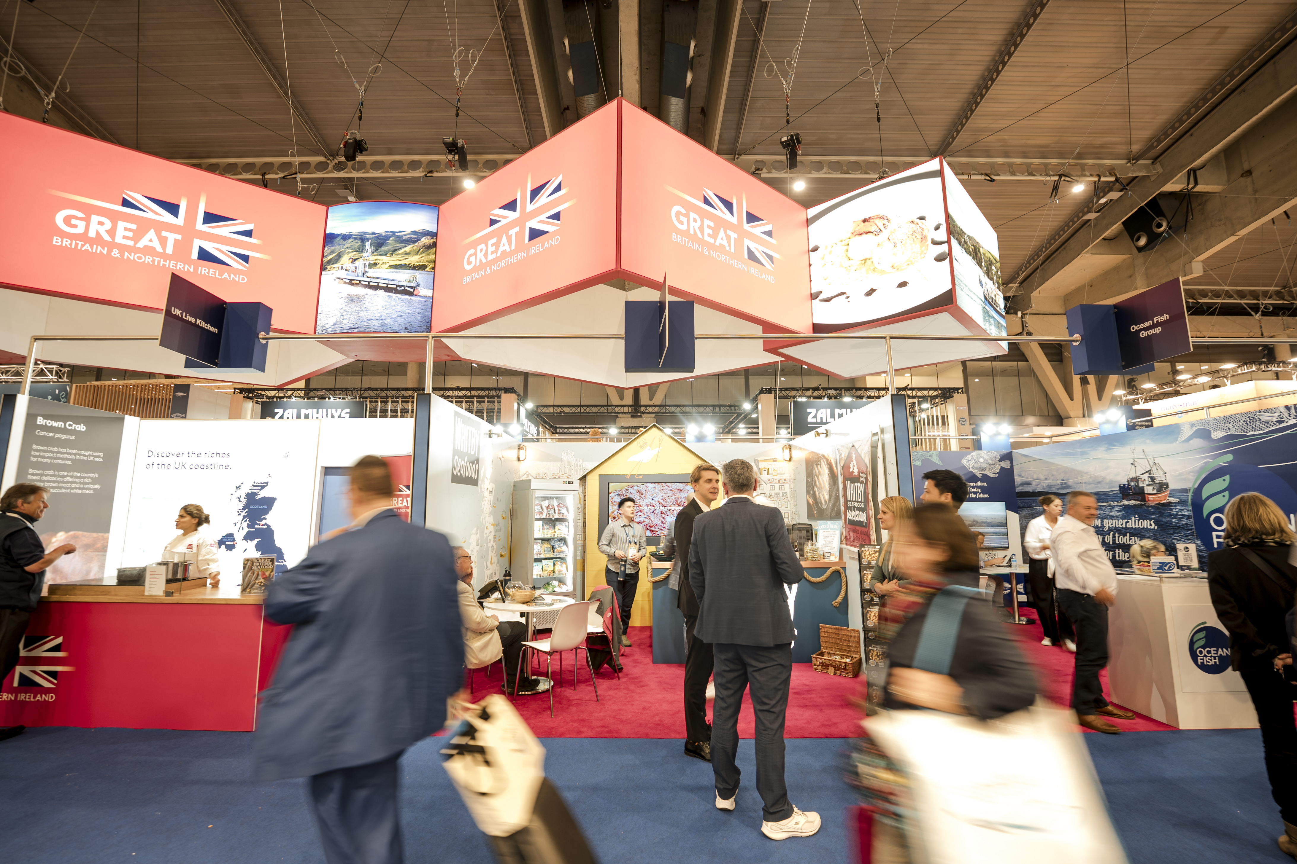 People walk past a trade show exhibition while other stand around chatting.